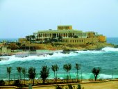 Außenansicht des Drago Casinos in Malta mit Meer und Palmen im Vordergrund